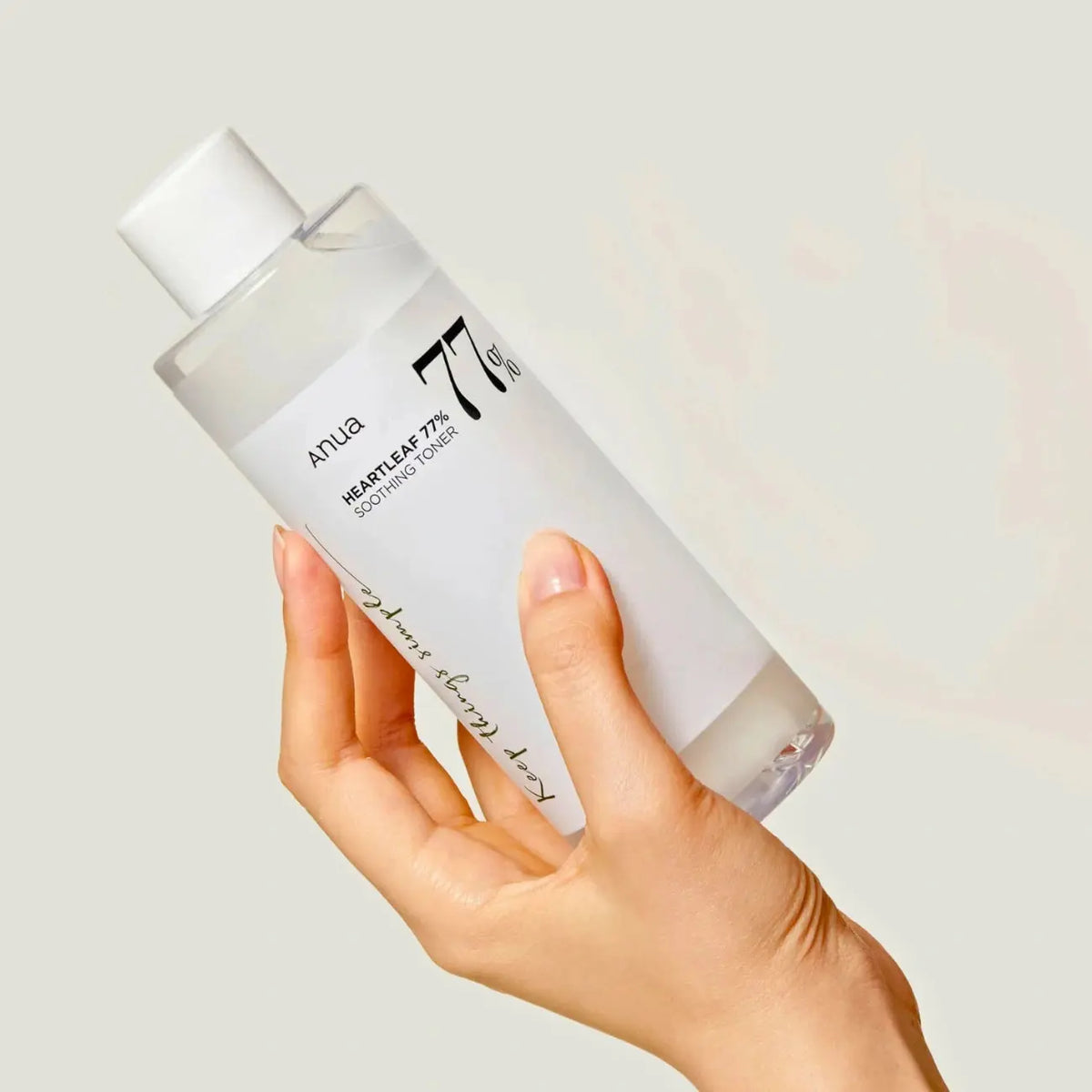 Hand holding a bottle of skincare product with a neutral background